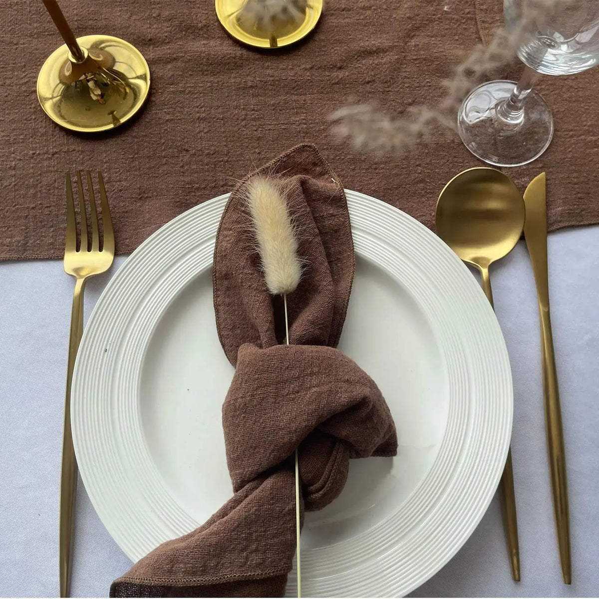 Une élégante table dressée avec des couverts dorés et un linge de table marron, évoquant une expérience de dîner raffinée.