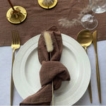 Une élégante table dressée avec des couverts dorés et un linge de table marron, évoquant une expérience de dîner raffinée.