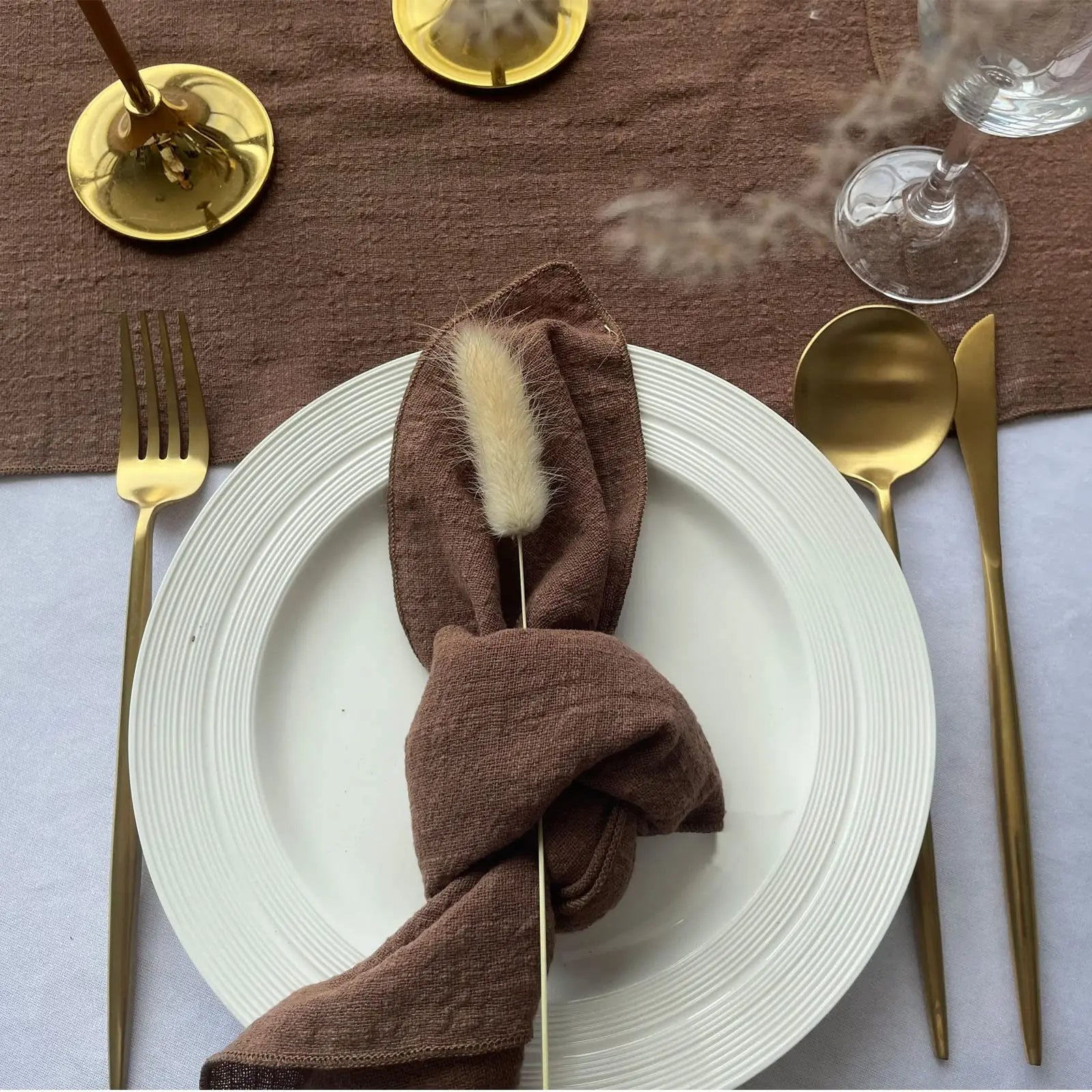 Une élégante table dressée avec des couverts dorés et un linge de table marron, évoquant une expérience de dîner raffinée.