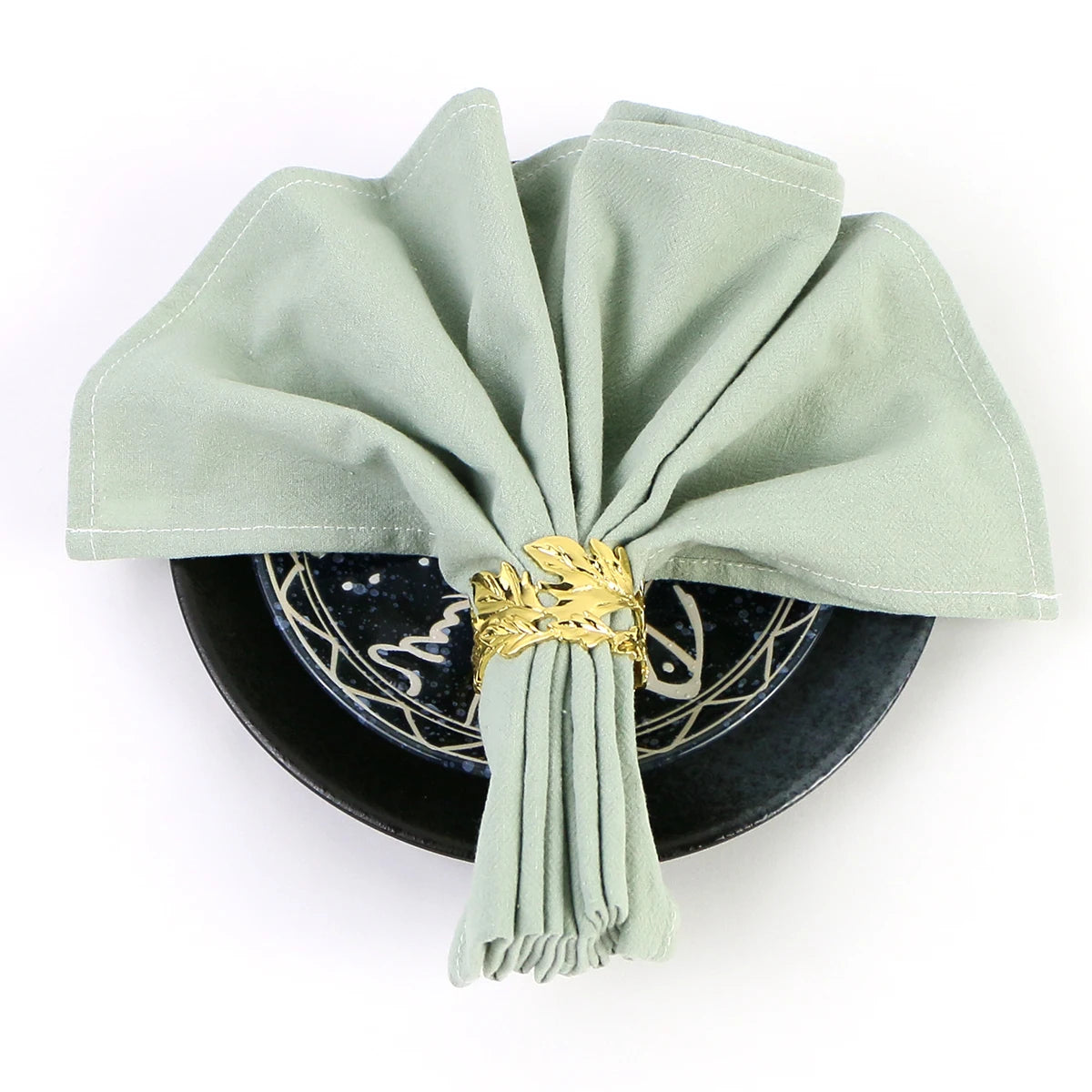 Une superbe décoration murale ronde en métal noir avec des motifs décoratifs et un noeud de tissu vert pastel rehaussé d'un ornement doré, créant un effet élégant et raffiné.