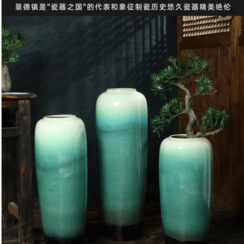Ce sont des vases en céramique de couleur vert dégradé, posés devant un petit arbre en pot, dans un décor sombre et boisé, dégageant une atmosphère zen.