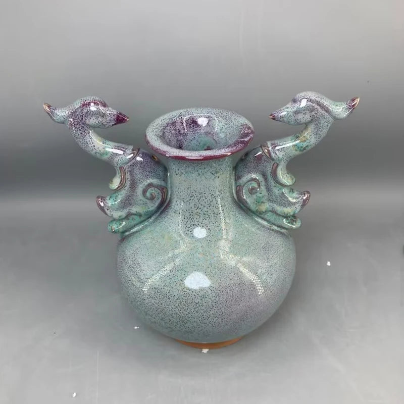 Vase en céramique artistique de forme abstraite avec des éléments décoratifs en forme de figures d'animaux, dans des tons de vert et de violet.