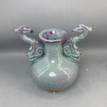 Vase en céramique artistique de forme abstraite avec des éléments décoratifs en forme de figures d'animaux, dans des tons de vert et de violet.
