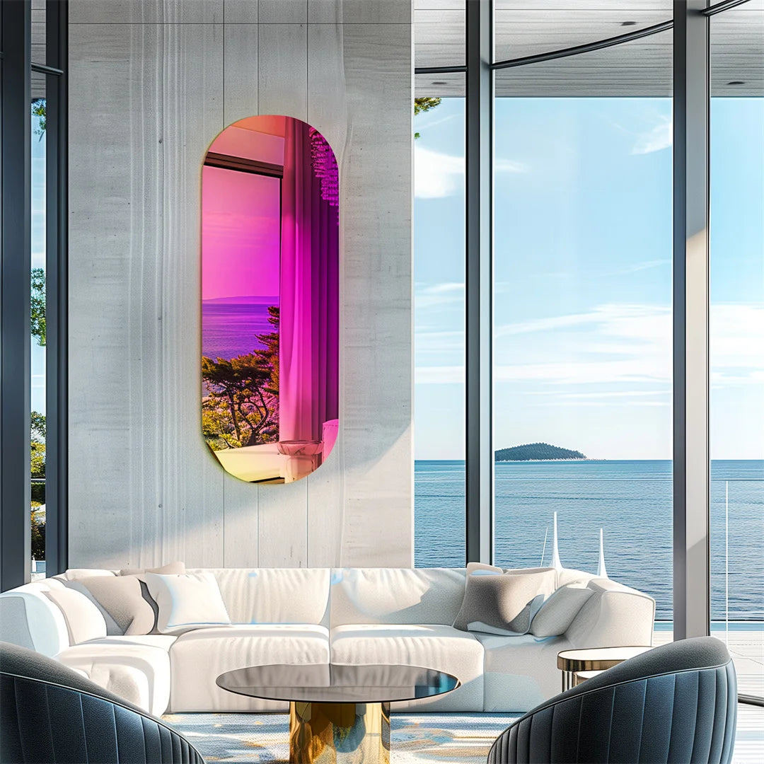 L'image montre un intérieur moderne avec de grandes fenêtres offrant une vue magnifique sur un paysage maritime. Un miroir ovale coloré en rose et jaune est accroché au mur, créant un accent visuel intéressant. Le mobilier comprend un canapé blanc et des fauteuils noirs, ainsi qu'une table basse ronde. L'ensemble crée une atmosphère élégante et relaxante.