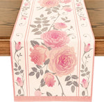 Chemin de table décoré de belles roses roses et de feuilles grises sur un fond blanc.