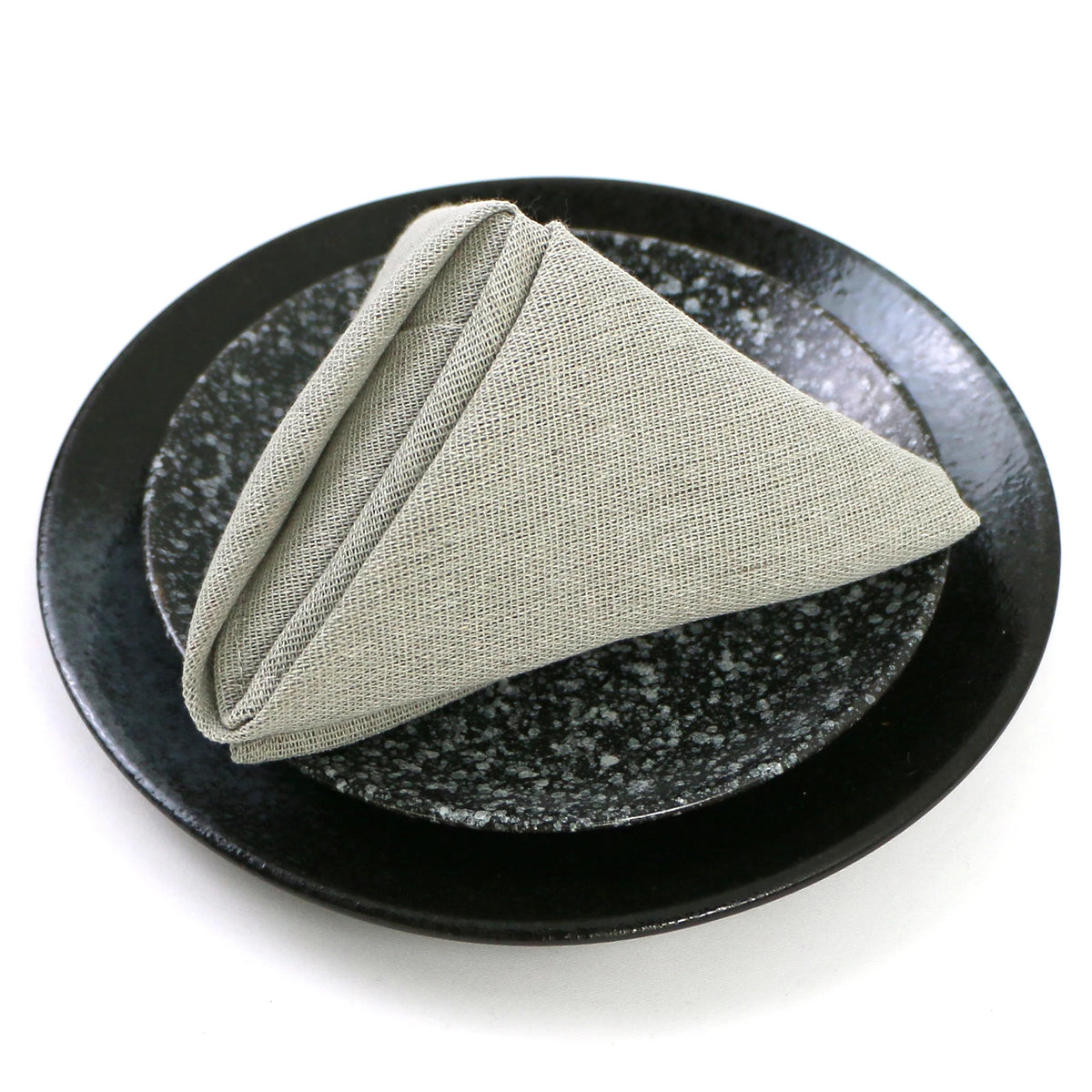 Une serviette beige pliée sur une assiette noire avec une surface texturée.