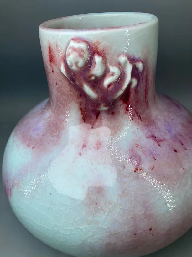 Un vase en céramique irrégulier aux teintes pastel et rougeâtres, avec des motifs abstraits et des reflets brillants.
