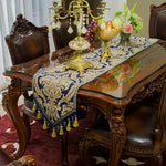 Table d'apparat richement décorée, avec des chandeliers dorés, des fleurs et des fruits, posée sur un tapis rouge et une nappe luxueuse dans un style classique et élégant.