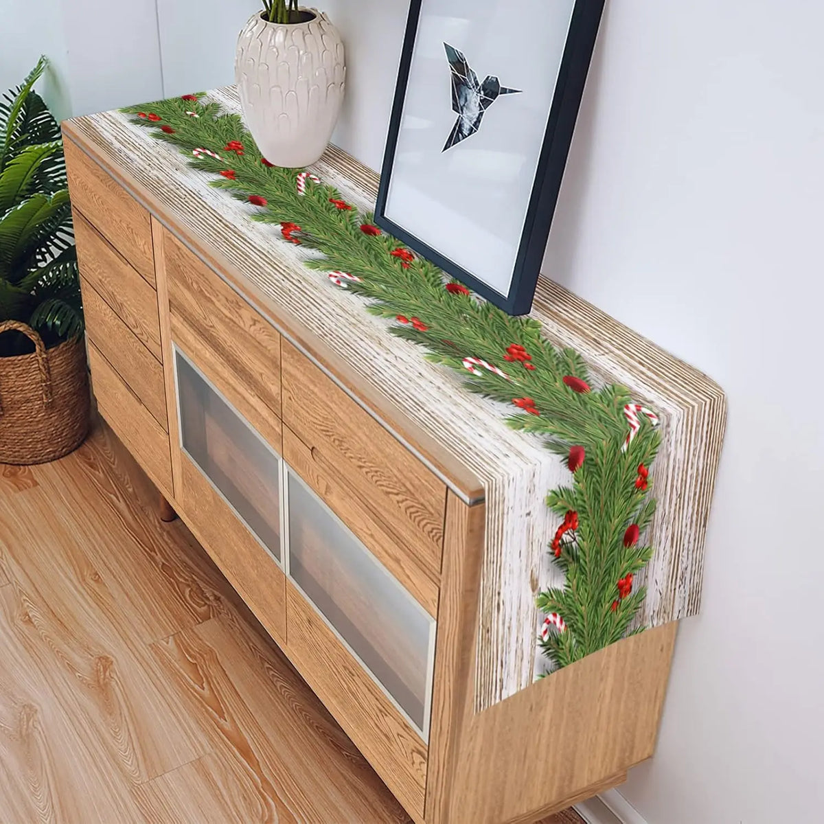 Un meuble en bois massif orné d'une guirlande de Noël verte et rouge, avec une fenêtre encadrée et une plante dans un vase, créant une atmosphère chaleureuse et festive.