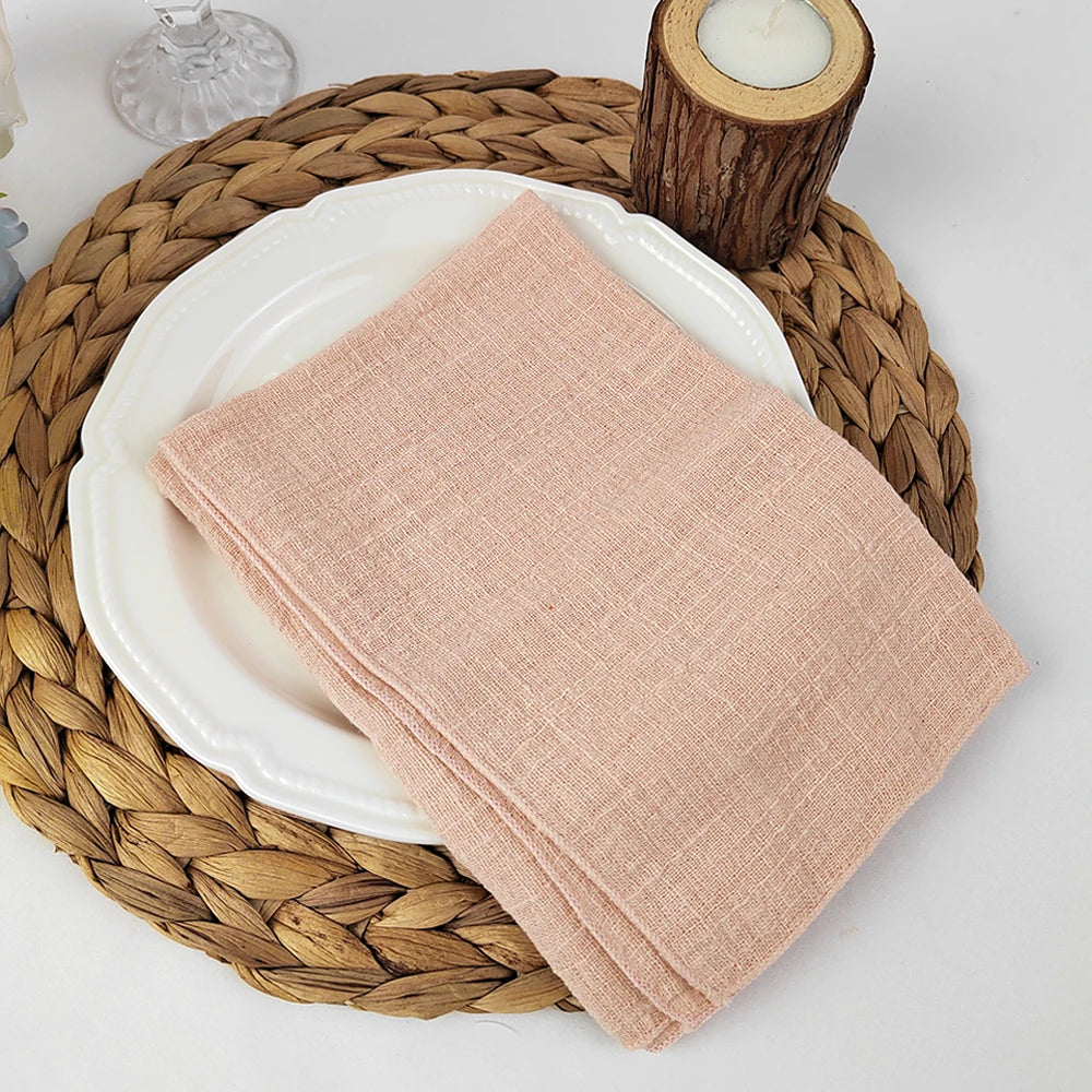 Une serviette en tissu rose clair posée sur une assiette blanche sur un tapis de table en fibres tressées.