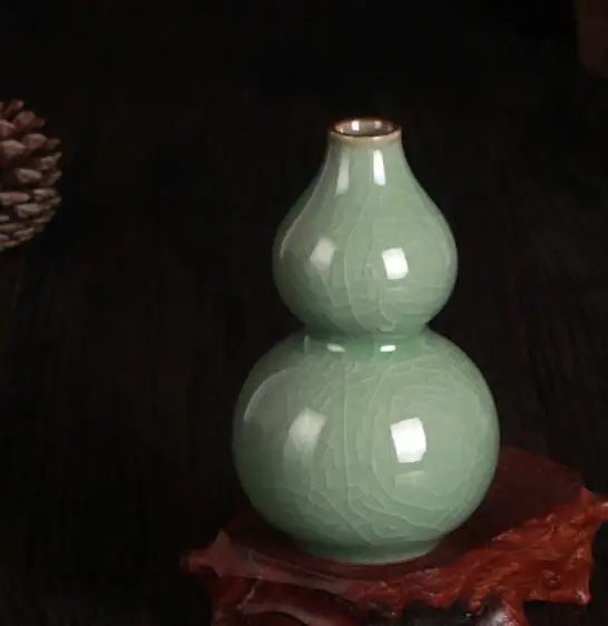 Un vase décoratif à double boule en céramique de couleur vert clair, posé sur un support en tissu rouge.