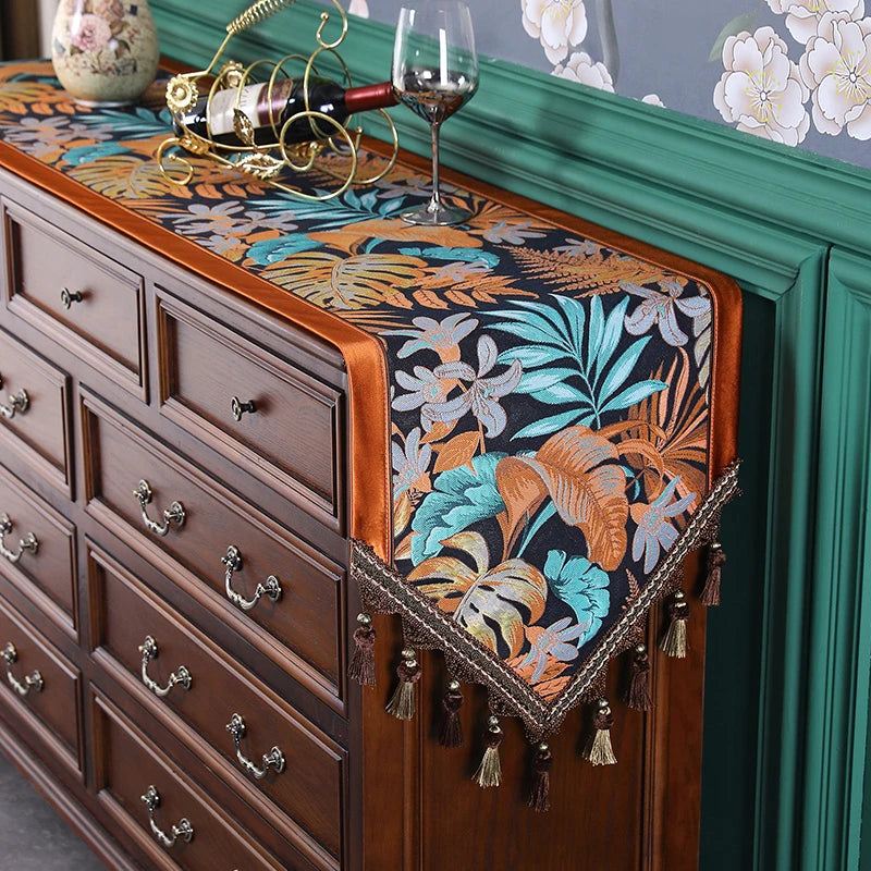Cette élégante commode en bois dispose d'un dessus peint à la main avec des motifs floraux tropicaux aux couleurs vives, complété par une élégante nappe décorée de glands, donnant une touche sophistiquée à cette pièce d'ameublement.