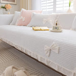 Un canapé blanc moelleux avec des coussins roses et des nœuds de dentelle blanche, donnant une atmosphère féminine et romantique dans cette pièce lumineuse et accueillante.