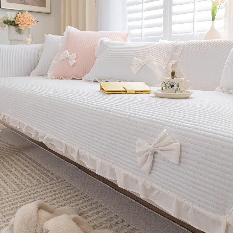 Un canapé blanc moelleux avec des coussins roses et des nœuds de dentelle blanche, donnant une atmosphère féminine et romantique dans cette pièce lumineuse et accueillante.