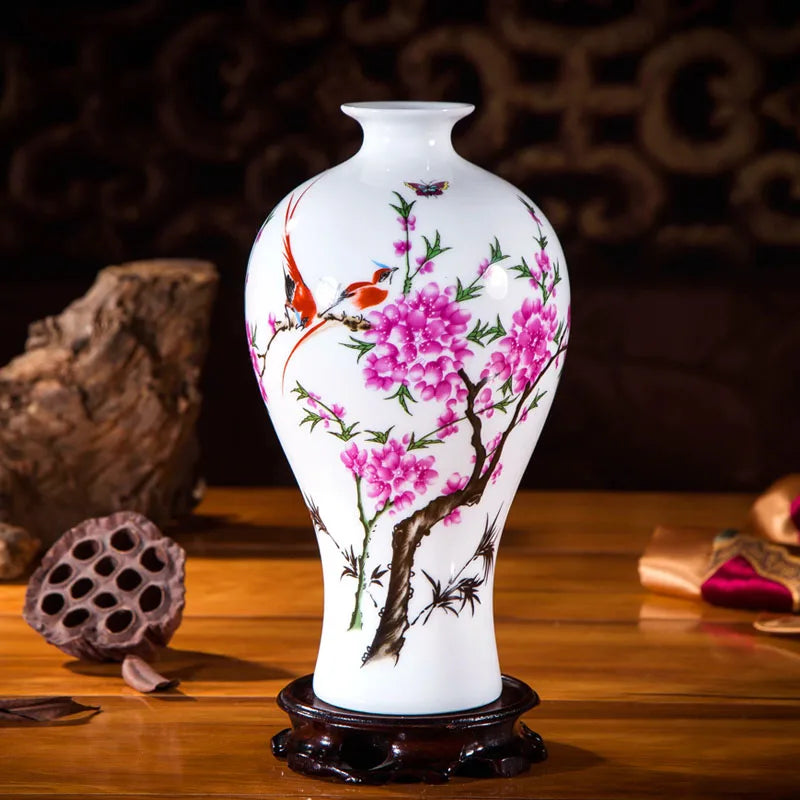 Vase en porcelaine blanche décoré de fleurs de prunier rose vif et d'oiseaux rouges, sur un socle en bois sombre.