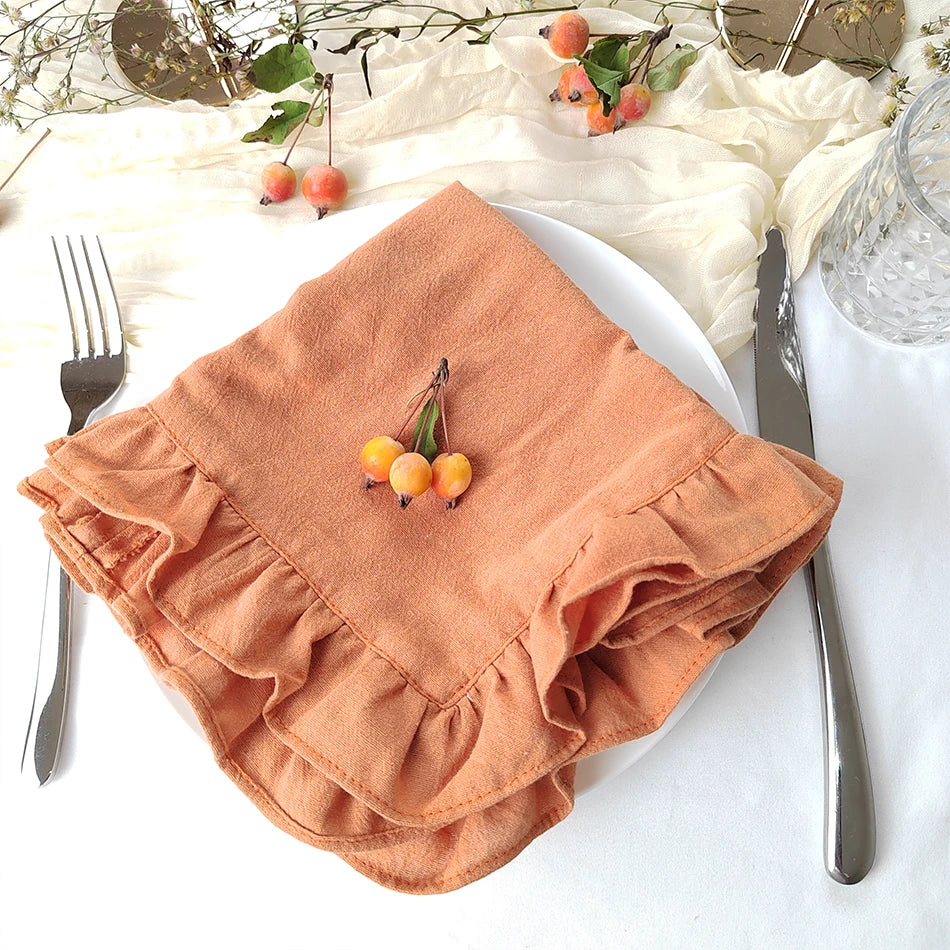 Une serviette de table en lin beige, décorée de baies rouges, posée sur une surface blanche avec des couverts et des fleurs.