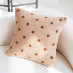 Coussin douillet beige à motifs pois marron posé sur un canapé blanc.