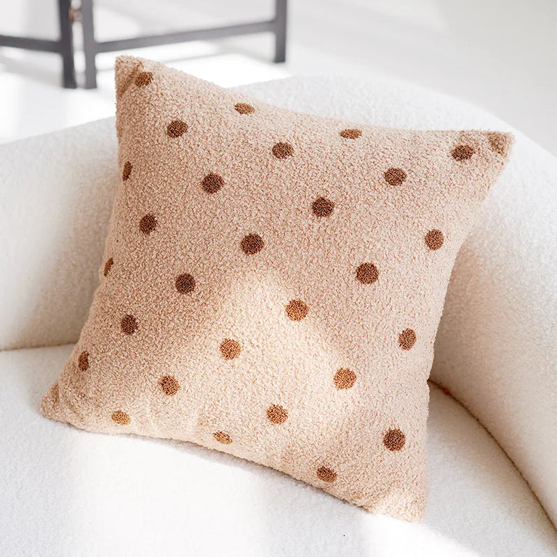 Coussin douillet beige à motifs pois marron posé sur un canapé blanc.