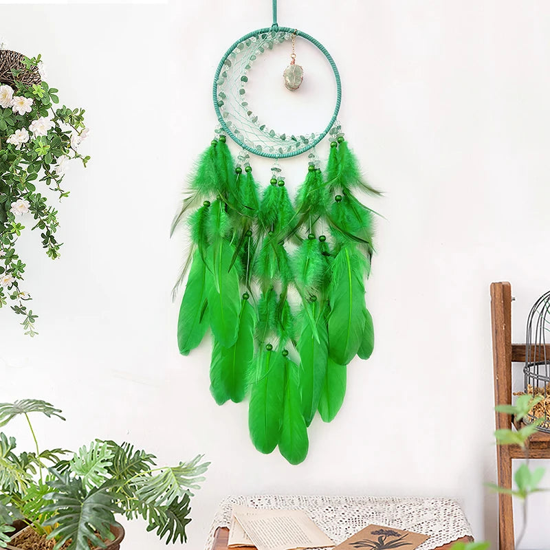 Attrape-rêves décoratif en plumes vertes suspendues à un cercle de métal bleu verdâtre, avec des pierres de cristal translucides, dans un intérieur lumineux avec des plantes vertes.