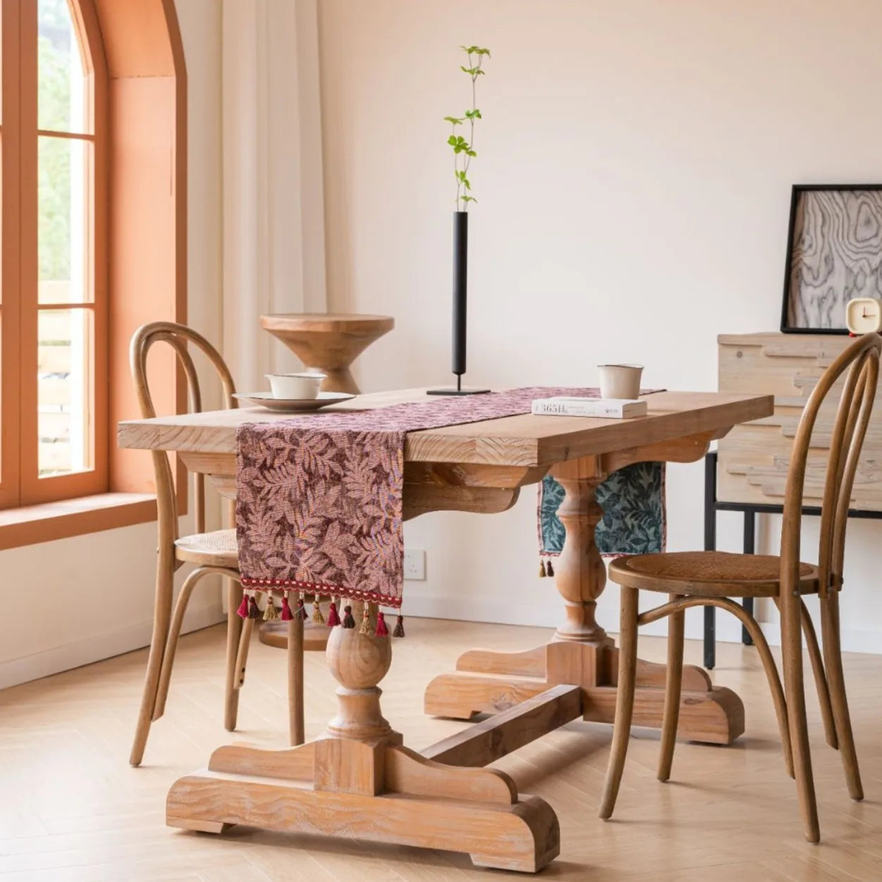 Une table en bois rustique avec un chemin de table coloré et un arrangement végétal élégant, créant une atmosphère chaleureuse et naturelle dans cette salle à manger.