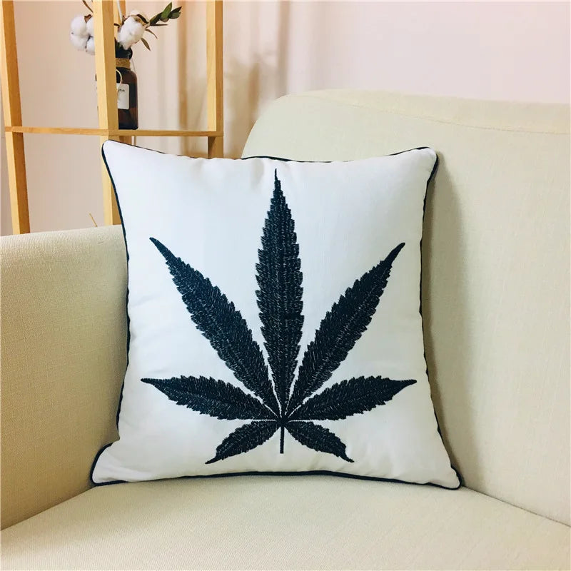 Coussin décoratif blanc avec l'emblème d'une feuille de cannabis noire, placé sur un canapé beige.