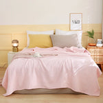 La chambre à coucher est meublée avec un lit douillet aux couleurs pastels, avec une couverture rose ornée de bandes blanches et un coussin gris, créant une ambiance chaleureuse et apaisante.