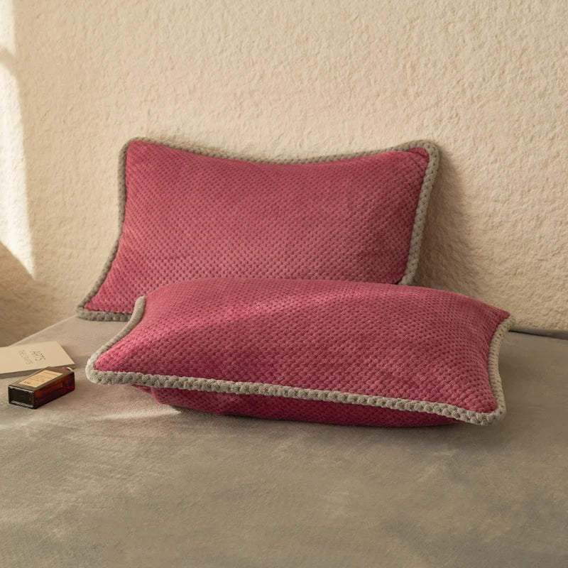 Deux coussins rectangulaires rouge foncé avec un bord gris, posés sur un canapé beige.