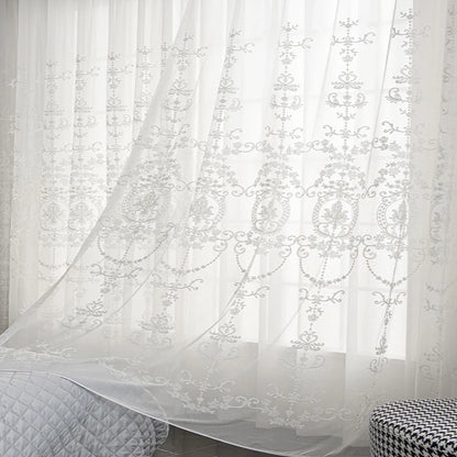 Voilage blanc transparent à motifs floraux élégants, flottant légèrement devant une fenêtre dans une chambre paisible.