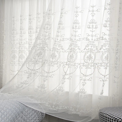 Voilage blanc transparent à motifs floraux élégants, flottant légèrement devant une fenêtre dans une chambre paisible.
