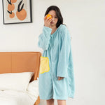 Une femme dans un long manteau moelleux à capuche vert menthe se tient dans une chambre avec un mur blanc et un cadre artistique.