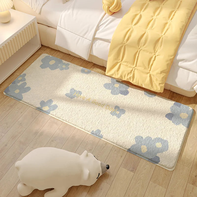 Tapis de sol de chambre à coucher avec un motif de fleurs bleues sur fond crème, placé à côté d'un lit avec un oreiller jaune et d'un jouet en forme d'ours blanc.