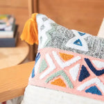 Coussin décoratif avec motifs géométriques colorés et frange jaune, sur un meuble en bois.