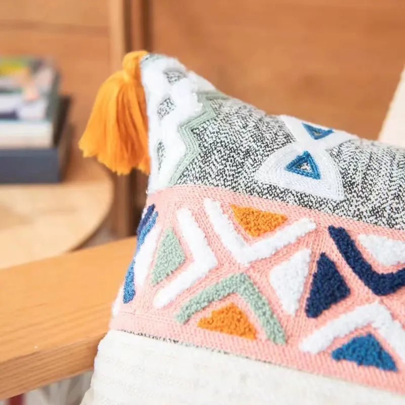 Coussin décoratif avec motifs géométriques colorés et frange jaune, sur un meuble en bois.