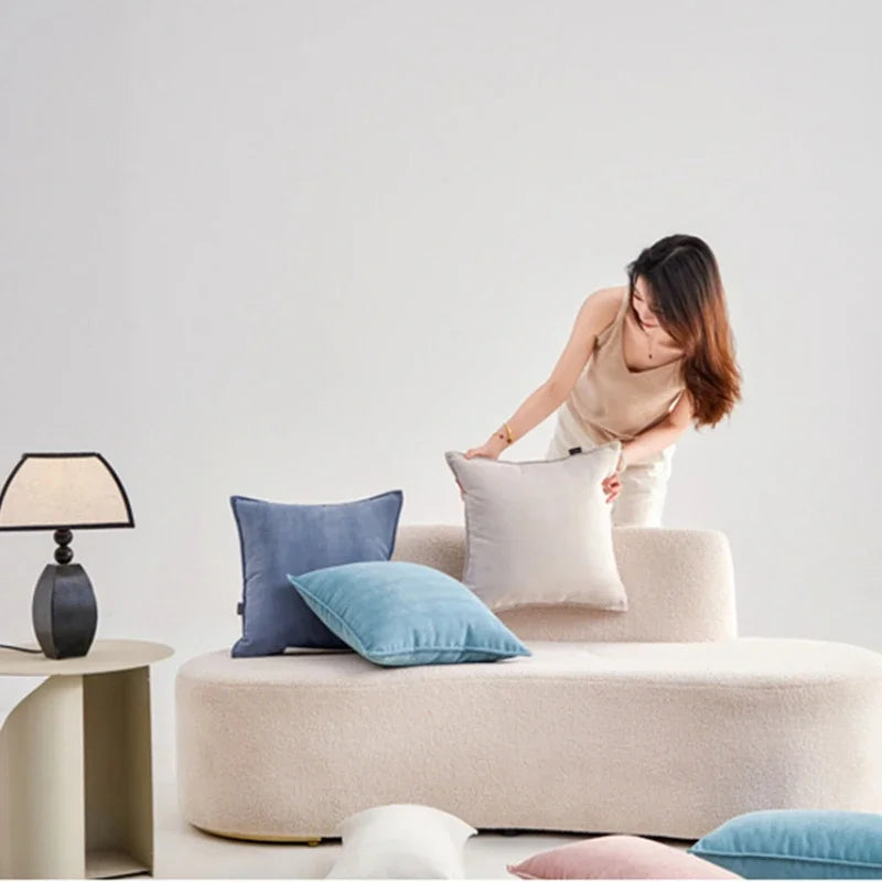 Une femme arrangeant des coussins décoratifs sur un canapé blanc dans un salon moderne avec une lampe de table.