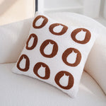 Un oreiller blanc avec des imprimés circulaires marron, offrant un aspect moderne et géométrique.