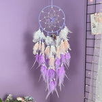 Un bel attrape-rêves décoratif en plumes blanches et violettes suspendu au mur, créant une atmosphère apaisante et mystique dans cette pièce violette.