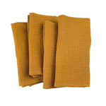 Des serviettes douces et texturées de couleur moutarde empilées sur un fond blanc.