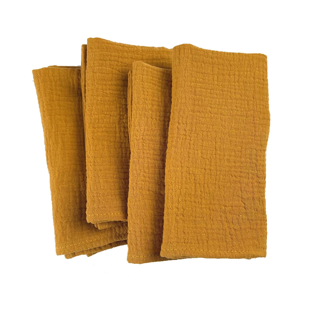 Des serviettes douces et texturées de couleur moutarde empilées sur un fond blanc.