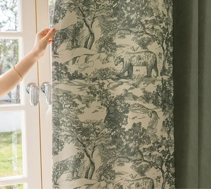 Femme tirant un rideau vert à motifs graphiques représentant une scène forestière avec des animaux.