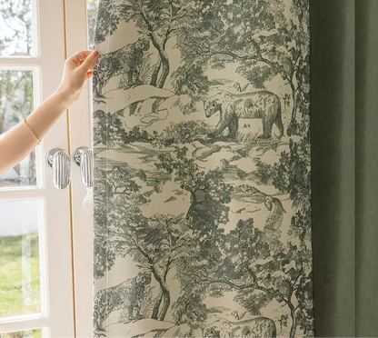 Femme tirant un rideau vert à motifs graphiques représentant une scène forestière avec des animaux.