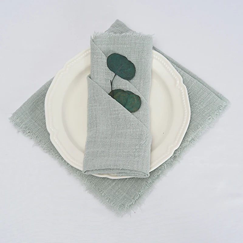 Des serviettes de table grises en lin avec des feuilles vertes décorant un service de table blanc sobre et élégant.