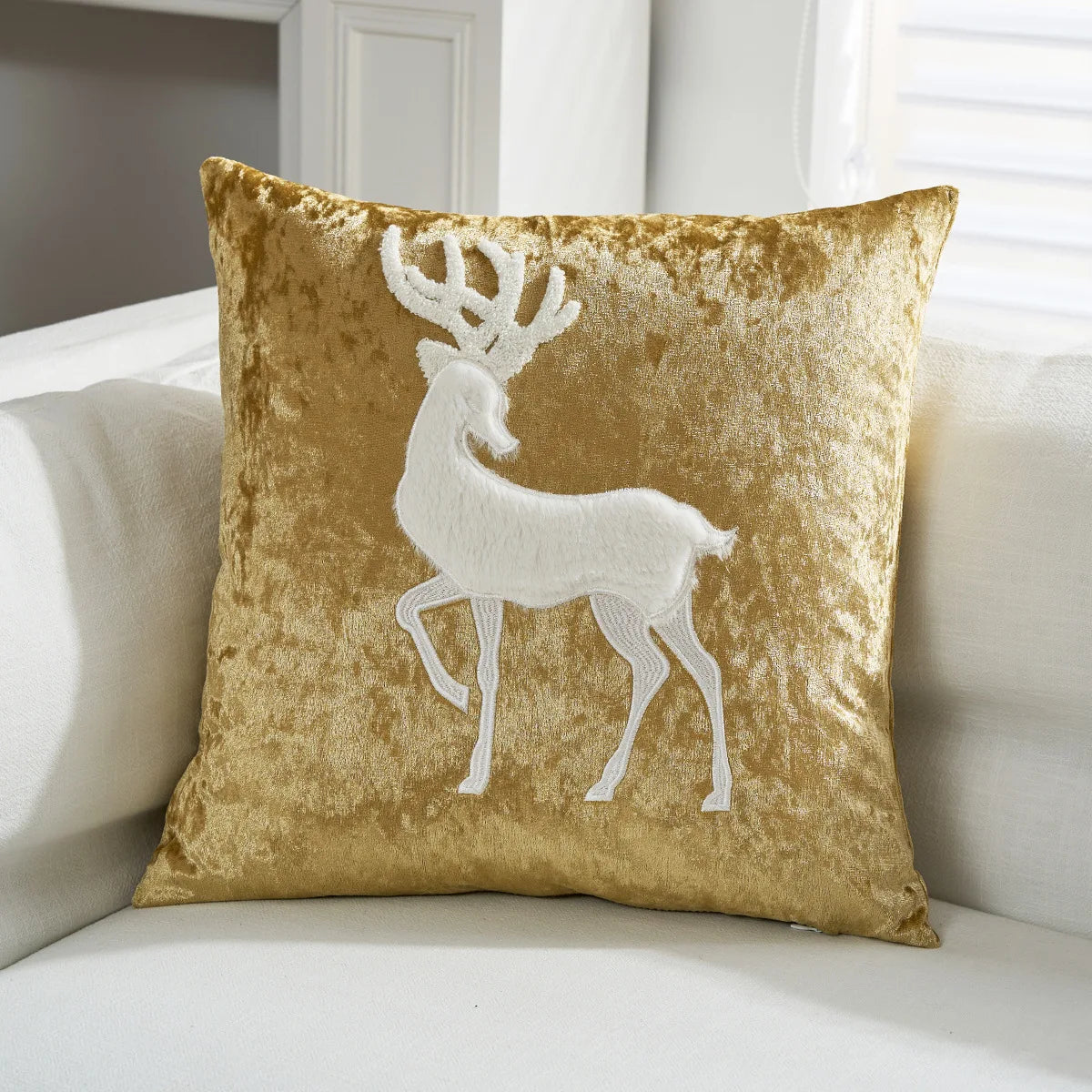 Un coussin doré avec un design de cerf stylisé en blanc.
