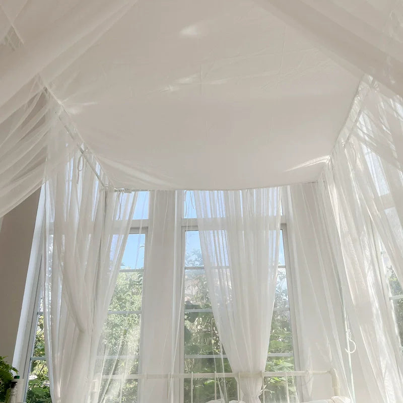 Une fenêtre baie vitrée aux rideaux transparents offrant une vue sur la nature verdoyante à l'extérieur.