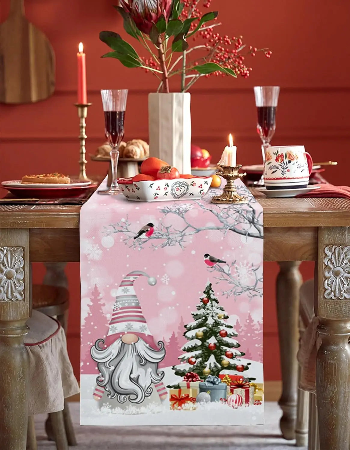 La table est magnifiquement décorée pour les fêtes, avec une nappe rose ornée de motifs hivernaux, un arbre de Noël décoré et une belle composition florale.