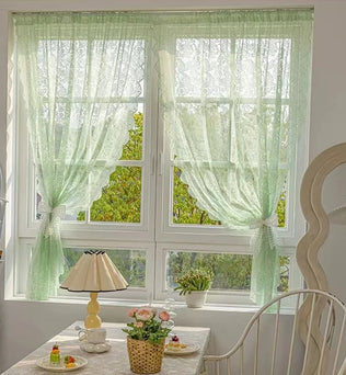 Voilage vert transparent en dentelle, installé sur une fenêtre blanche dans une salle à manger cosy au style vintage fleuri.