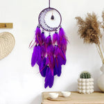 Un magnifique attrape-rêves violet suspendu, orné de plumes aux teintes profondes et colorées, créant une décoration murale élégante et bohème.