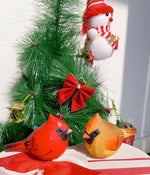 Ornements de Noël colorés, y compris un bonhomme de neige en tricot rouge et blanc, des oiseaux en bois peints en rouge et orange et des décorations vertes et rouges sur un arbre de Noël.