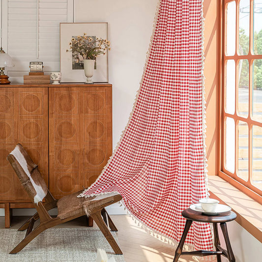 Rideau à carreaux rouges et blancs dans un salon moderne, apportant une touche de charme rustique. Ce rideau intemporel illumine la pièce en filtrant la lumière naturelle près d'un fauteuil en bois. Idéal pour une décoration intérieure chaleureuse et accueillante.