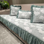 Ensemble de literie décoratif avec motif floral gris clair et vert menthe sur un canapé en peluche.