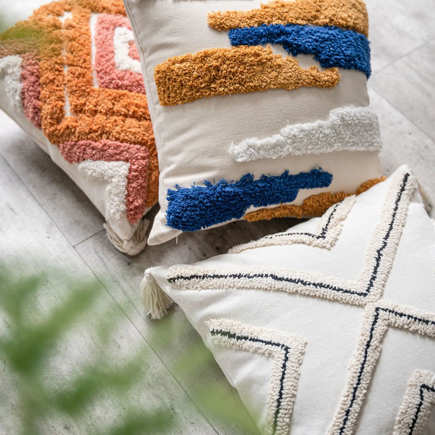 Coussins décoratifs multicolores avec motifs géométriques et textures moelleuses sur un sol en bois clair.